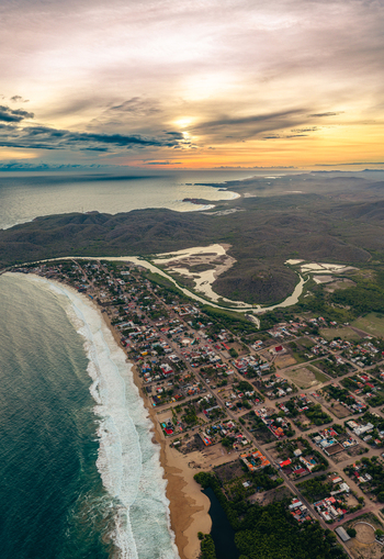 Aerial view of Playa Punta Perula with its coastal town sandy beach and ocean waves under a golden sunset in Perula Jalisco Mexico. Aerial view of Playa Punta Perula with its coastal town sandy beach and ocean waves under a golden sunset in Perula Jalisco Mexico.