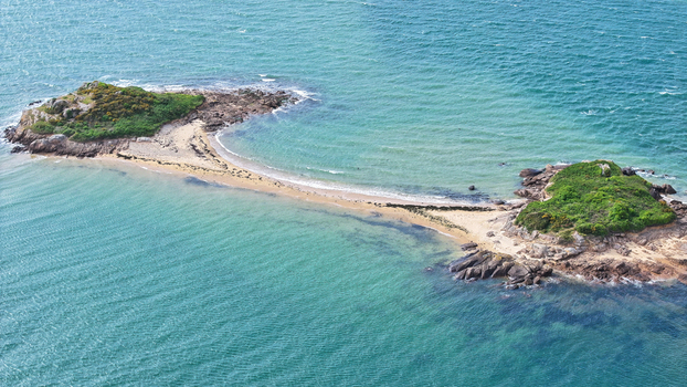 Aerial view of two small rocky islands covered in green vegetation connected by a narrow sandy beach strip surrounded by turquoise sea water Carantec Brittany France. Aerial view of two small rocky islands covered in green vegetation connected by a narrow sandy beach strip surrounded by turquoise sea water Carantec Brittany France.