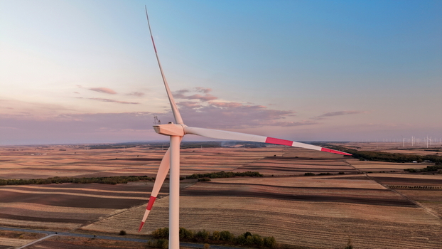 Aerial view of a large wind turbine standing in a vast agricultural field during golden hour in Vladimirovac Vojvodina Serbia.