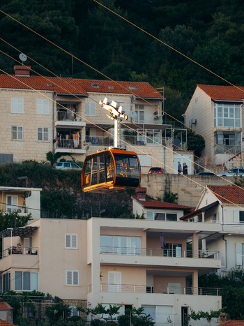 View of the orange Dubrovnik Cable Car cabin with people inside ascending over residential houses with red tiled roofs in Dubrovnik Dubrovnik Neretva County Croatia. View of the orange Dubrovnik Cable Car cabin with people inside ascending over residential houses with red tiled roofs in Dubrovnik Dubrovnik Neretva County Croatia.
