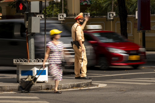 Hanoi Ha Noi Vietnam 11 November 2025 View of a traffic police officer in uniform directing traffic at a busy intersection with a blurred pedestrian and passing vehicles.