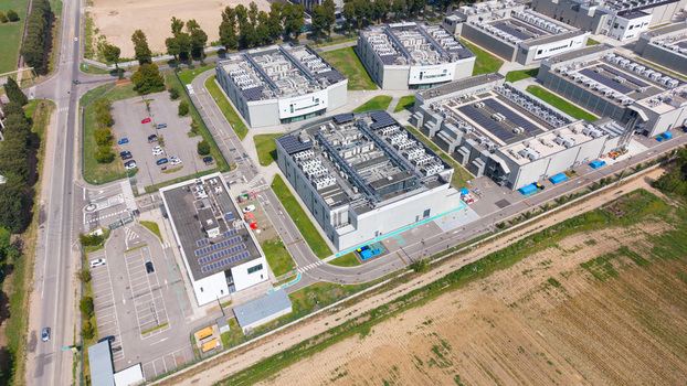 Aerial view of a modern data center campus with industrial buildings featuring rooftop solar panels parking areas and surrounding fields in Milan Lombardy Italy. Aerial view of a modern data center campus with industrial buildings featuring rooftop solar panels parking areas and surrounding fields in Milan Lombardy Italy.