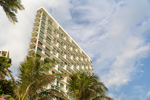 View of a modern high rise hotel building with white balconies and glass windows framed by tropical palm trees under a blue sky in Galle Southern Province Sri Lanka.