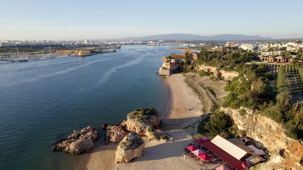 Aerial view of the Ferragudo coastline featuring the historic Castelo de Sao Joao do Arade sandy beach rocky formations and a restaurant in Ferragudo Faro District Portugal.