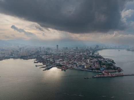 Aerial view of the historic skyline waterfront and harbor under dramatic dark storm clouds with sunlight breaking through in George Town Penang Malaysia. Aerial view of the historic skyline waterfront and harbor under dramatic dark storm clouds with sunlight breaking through in George Town Penang Malaysia.