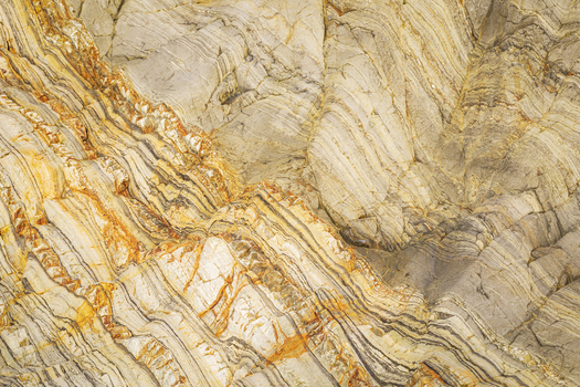 View of the intricate geological layers and folded rock formations at Silence Beach featuring vibrant orange and beige mineral veins in Asturias Asturias Spain.