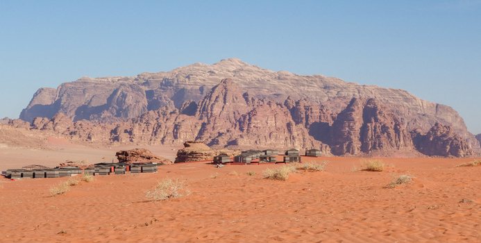 View of a Bedouin camp with traditional tents set against the dramatic red sandstone mountains and vast sand dunes of the Wadi Rum Desert in Wadi Rum Village Aqaba Governorate Jordan. View of a Bedouin camp with traditional tents set against the dramatic red sandstone mountains and vast sand dunes of the Wadi Rum Desert in Wadi Rum Village Aqaba Governorate Jordan.