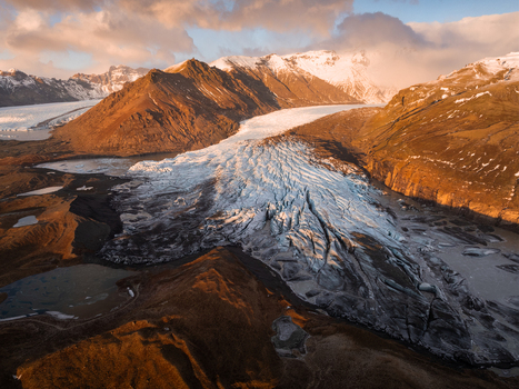Aerial view of Svinafellsjokull glacier with rugged ice formations deep crevasses and surrounding mountains under golden hour light in Hornafjordur Iceland. Aerial view of Svinafellsjokull glacier with rugged ice formations deep crevasses and surrounding mountains under golden hour light in Hornafjordur Iceland.