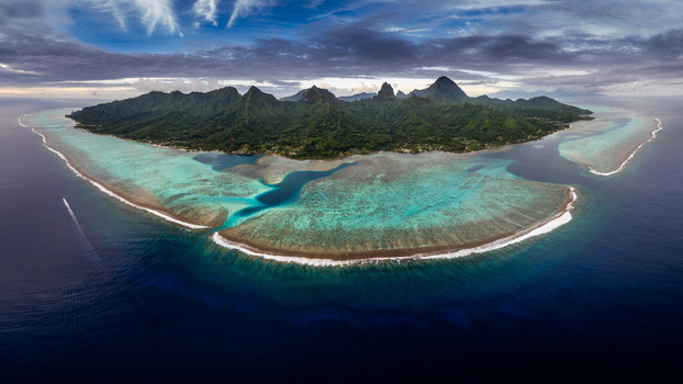 Aerial view of the lush volcanic peaks and turquoise coral lagoon of Moorea island under a dramatic sky in Moorea Maiao Windward Islands French Polynesia. Aerial view of the lush volcanic peaks and turquoise coral lagoon of Moorea island under a dramatic sky in Moorea Maiao Windward Islands French Polynesia.