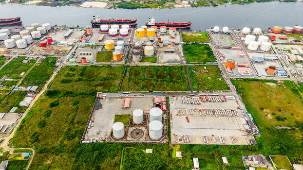 Aerial view of the industrial oil storage facility with large cylindrical tanks rows of parked tanker trucks and cargo ships docked along the waterway in Satellite Town Lagos Lagos Nigeria.