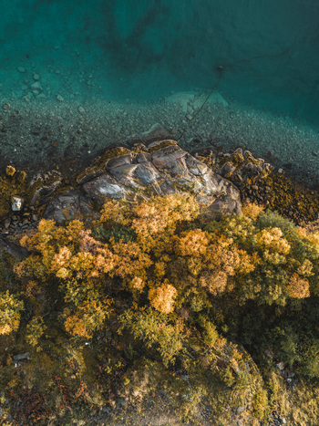 Aerial view of the rocky coastline of Senja with turquoise water and vibrant autumn foliage in Senja Troms Norway.
