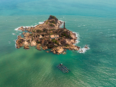 Aerial view of Ke Ga Lighthouse on a rocky island surrounded by turquoise sea with a fish farm in the water in Vietnam. Aerial view of Ke Ga Lighthouse on a rocky island surrounded by turquoise sea with a fish farm in the water in Vietnam.