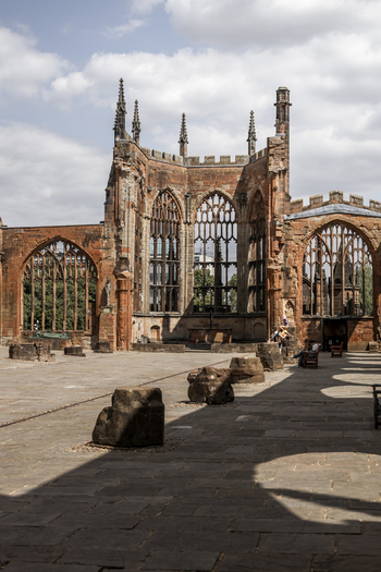 View of the ruins of the old Coventry Cathedral featuring Gothic stone arches traceried windows and a paved courtyard under a blue sky in Coventry England United Kingdom.