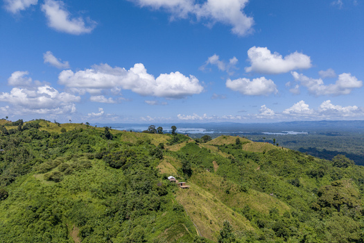 Aerial view of Shita Pahar featuring lush green hills small structures and dense vegetation under a blue sky overlooking the distant Kaptai Lake in Kaptai Chittagong Division Bangladesh. Aerial view of Shita Pahar featuring lush green hills small structures and dense vegetation under a blue sky overlooking the distant Kaptai Lake in Kaptai Chittagong Division Bangladesh.