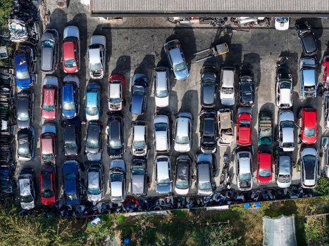 Aerial view of a car scrapyard with rows of abandoned and wrecked vehicles parked in an organized lot under bright sunlight Settimo Torinese Piedmont Italy.