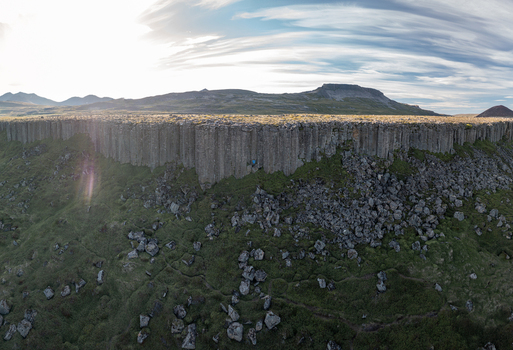 Aerial view of Gerduberg Cliffs featuring hexagonal basalt columns rising above a grassy slope with scattered rocks under a bright sky Raudhamelur Eyja og Miklaholtshr Iceland. Aerial view of Gerduberg Cliffs featuring hexagonal basalt columns rising above a grassy slope with scattered rocks under a bright sky Raudhamelur Eyja og Miklaholtshr Iceland.