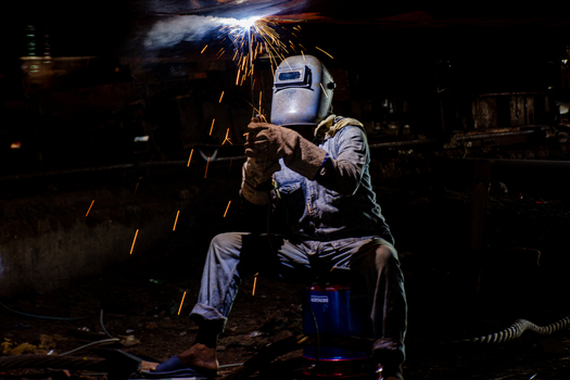 Keraniganj Bangladesh 11 September 2022 View of a welder working on a ship s hull at the Shipyard Dhaka with bright sparks flying and protective gear in a dark industrial setting.
