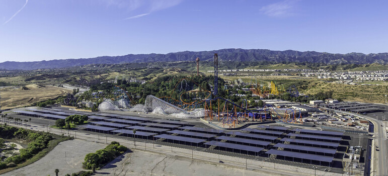 Aerial view of Six Flags Magic Mountain featuring colorful roller coasters and a large solar panel parking lot with hills under a clear blue sky in Los Angeles County California United States.