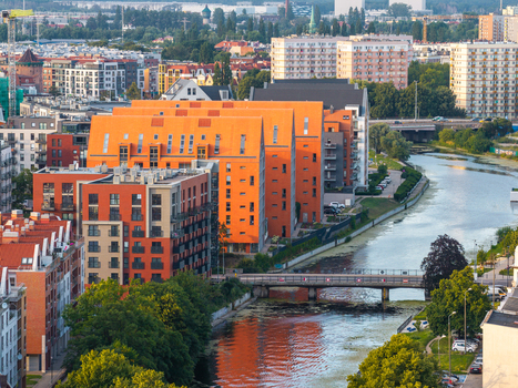 Aerial view of modern orange apartment buildings along a canal with a bridge and lush trees in Gdansk Pomeranian Voivodeship Poland. Aerial view of modern orange apartment buildings along a canal with a bridge and lush trees in Gdansk Pomeranian Voivodeship Poland.