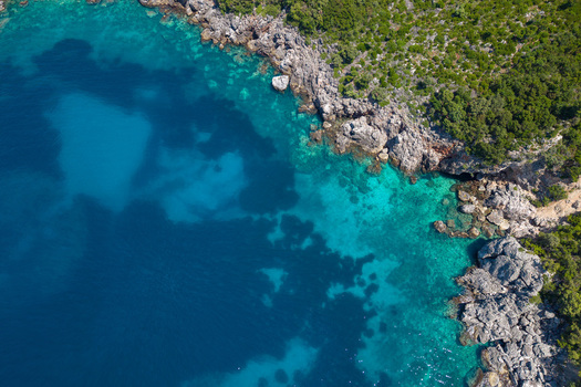Aerial view of Aquarium Beach with crystal clear turquoise waters rugged grey cliffs and lush green Mediterranean vegetation in Jala Vlore County Albania.