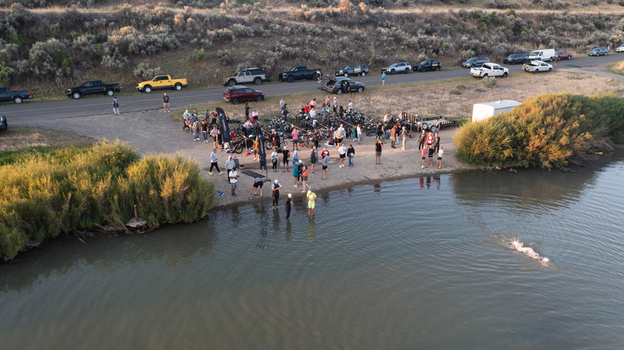 Aerial view of a group of people preparing for a swim in the river with parked vehicles on the shore in Cody Wyoming United States.