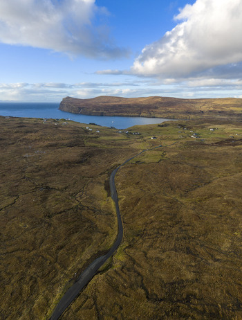Aerial view of a winding road through rugged moorland leading to the coastal village of Milovaig and Loch Pooltiel under a cloudy sky Milovaig Scotland United Kingdom.