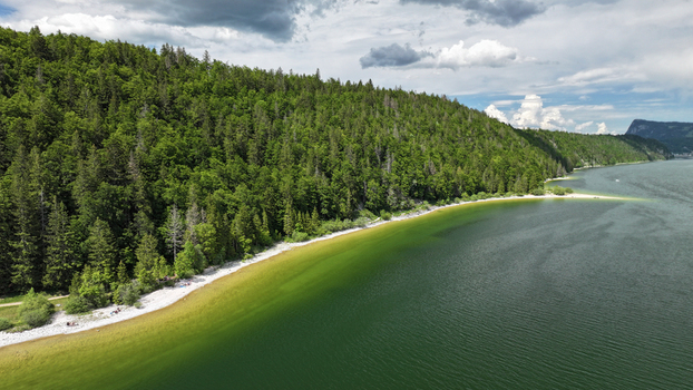Aerial view of the serene Lac de Joux reflecting the verdant forests and dramatic cliffs under a sky of scattered clouds Le Lieu Vaud Switzerland.