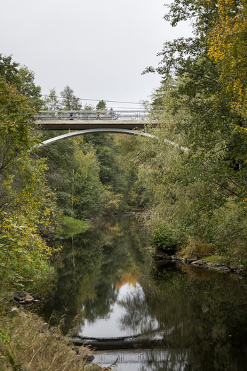 View of a concrete arch bridge spanning a calm river surrounded by lush autumn trees in Jyvaskyla Central Finland Finland.