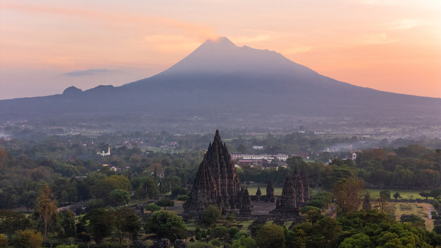 Aerial view of Prambanan Temple with Mount Merapi volcano in the background at sunrise surrounded by lush greenery in Kecamatan Prambanan Daerah Istimewa Yogya Indonesia.