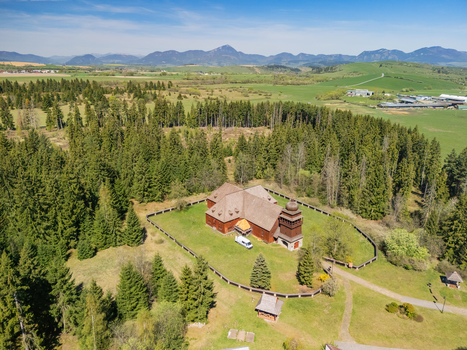 Aerial view of the Wooden Articular Church of Svaty Kriz surrounded by lush evergreen forests and rolling hills under a clear blue sky in Svaty Kriz Zilinsky kraj Slovakia.