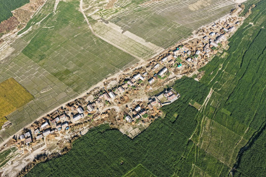 Aerial view of a rural village surrounded by lush green agricultural fields dirt paths and small residential structures in Joypurhat Rajshahi Division Bangladesh. Aerial view of a rural village surrounded by lush green agricultural fields dirt paths and small residential structures in Joypurhat Rajshahi Division Bangladesh.