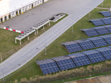 Aerial view of a solar panel farm adjacent to a large industrial warehouse with loading docks and HVAC units in Poland. Aerial view of a solar panel farm adjacent to a large industrial warehouse with loading docks and HVAC units in Poland.