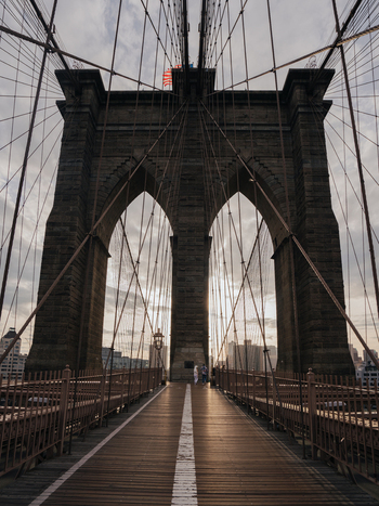 View of the iconic Brooklyn Bridge with its stone arches steel cables and wooden pedestrian walkway under a cloudy sky in New York New York United States.