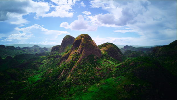 Aerial view of lush green mountains and valleys under a partly cloudy sky creating a vibrant contrast between the verdant landscape and the rocky peaks Vi&ntilde;ales Cuba.