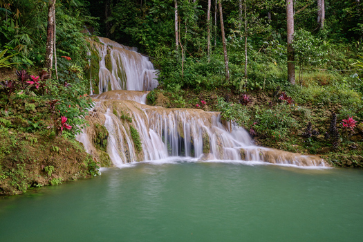 View of Air Terjun Kuncung Mas waterfall cascading over limestone rocks into a turquoise pool surrounded by lush tropical forest in Kecamatan Girimulyo Daerah Istimewa Yogya Indonesia. View of Air Terjun Kuncung Mas waterfall cascading over limestone rocks into a turquoise pool surrounded by lush tropical forest in Kecamatan Girimulyo Daerah Istimewa Yogya Indonesia.