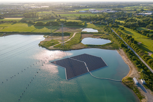 Aerial view of the floating photovoltaic system on a lake surrounded by green fields and power lines in Bensheim Hessen Germany. Aerial view of the floating photovoltaic system on a lake surrounded by green fields and power lines in Bensheim Hessen Germany.