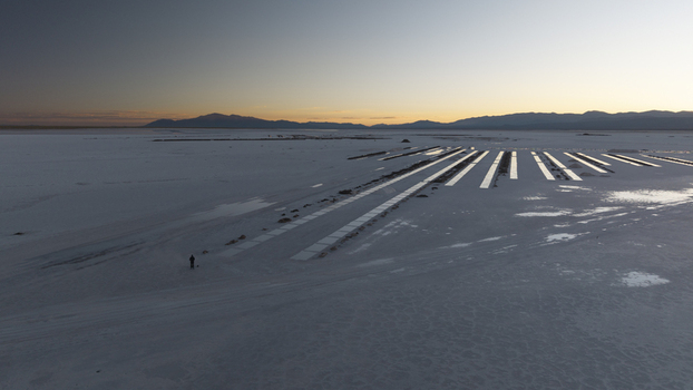 Aerial view of Salinas Grandes salt flats at sunset with long shadows and a lone person standing on the white salt crust in La Poma Department Salta Province Argentina. Aerial view of Salinas Grandes salt flats at sunset with long shadows and a lone person standing on the white salt crust in La Poma Department Salta Province Argentina.