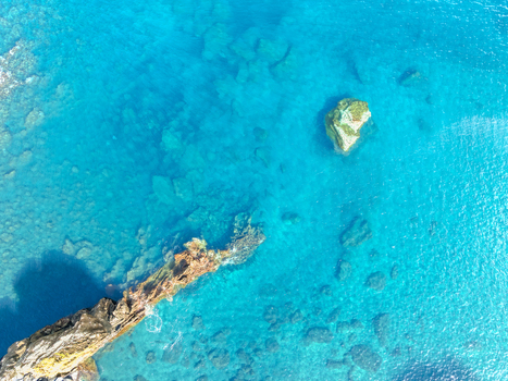 Aerial view of crystal clear turquoise water with submerged volcanic rocks and a rugged coastline Ribeira Grande Azores Portugal.