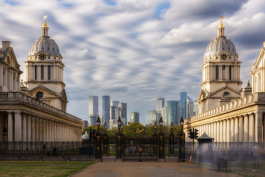 View of the historic Old Royal Naval College with its iconic twin domes and colonnades framing the distant Canary Wharf skyline in London England United Kingdom.