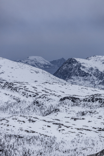 View of snowy mountain peaks and arctic wilderness under a moody overcast sky in Kvaloya Troms Norway.
