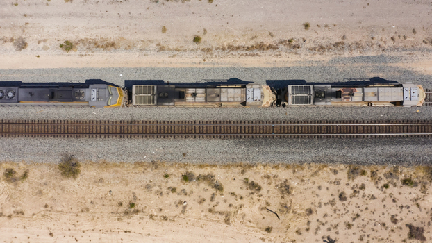 Aerial view of a freight train moving along tracks through an arid desert landscape with gravel ballast and sparse vegetation in the United States.