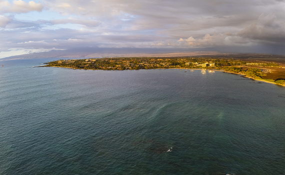 Aerial view of Waikoloa Beach featuring luxury resorts along the turquoise coastline with volcanic mountains under a soft sunset sky in Waikoloa Village Hawaii United States.