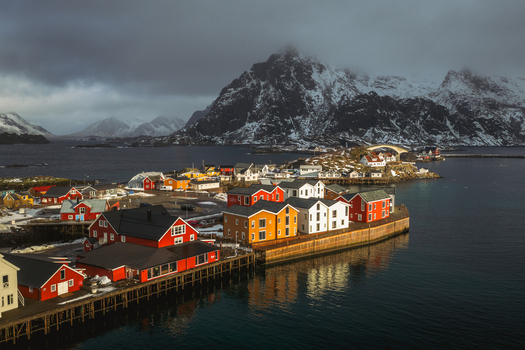 Aerial view of colorful houses nestled on the water s edge contrasting with the snow capped mountains in the background Henningsv&aelig;r Nordland Norway.