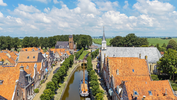Aerial view of the historic town of Sloten featuring a canal with a traditional sailing boat red tiled rooftops and lush green trees in Sloten Friesland Netherlands.