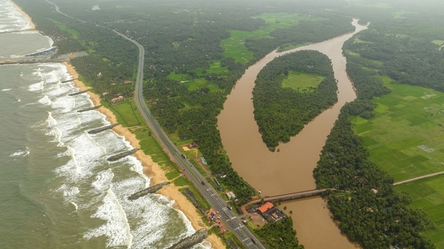 Aerial view of Maravanthe beach where the Arabian Sea and the Souparnika River run parallel separated by a highway with lush green fields and palm trees in Maravanthe Karnataka India. Aerial view of Maravanthe beach where the Arabian Sea and the Souparnika River run parallel separated by a highway with lush green fields and palm trees in Maravanthe Karnataka India.