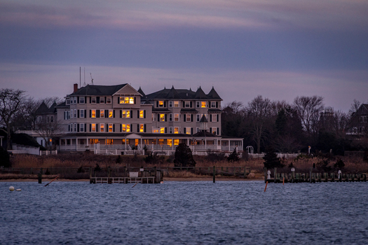 View of the historic Harbor View Hotel with glowing windows at twilight overlooking the waterfront and wooden piers in Edgartown Massachusetts United States.