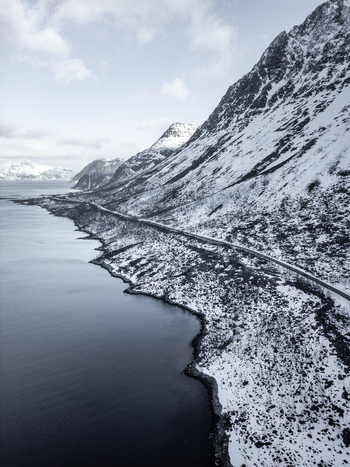 Aerial view of Grotfjord with a winding coastal road along snow covered mountains and dark water Tromvik Troms Norway. Aerial view of Grotfjord with a winding coastal road along snow covered mountains and dark water Tromvik Troms Norway.