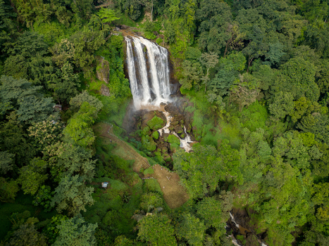 Aerial view of Curug Sewu Waterfall cascading down rocky cliffs surrounded by dense tropical forest and lush greenery in Kecamatan Patean Jawa Tengah Indonesia.