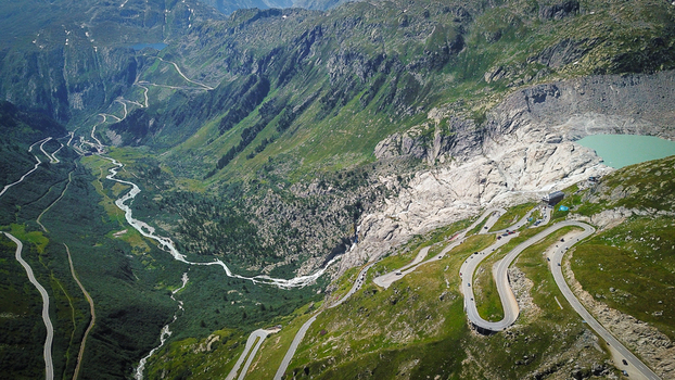 Aerial view of Furka Pass with its iconic winding hairpin turns the Rhone Glacier and a turquoise mountain lake nestled in the Swiss Alps near Obergoms Valais Switzerland. Aerial view of Furka Pass with its iconic winding hairpin turns the Rhone Glacier and a turquoise mountain lake nestled in the Swiss Alps near Obergoms Valais Switzerland.