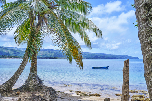 View of a tropical beach with palm trees clear blue water and a small boat floating near the shore in Santo Domingo Distrito Nacional Dominican Republic. View of a tropical beach with palm trees clear blue water and a small boat floating near the shore in Santo Domingo Distrito Nacional Dominican Republic.